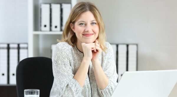Front view portrait of a businesswoman posing looking at you on a desk at office