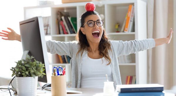 Shot of happy young business woman having fun and holding red apple over her head in the office.